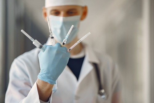 Person in White Dress Shirt With Face Mask Holding Four Syringes