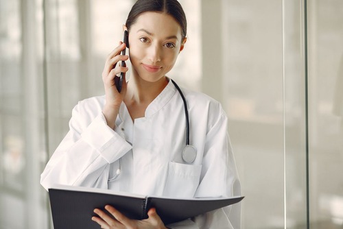 Positive doctor in medical uniform talking on cellphone in clinic corridor