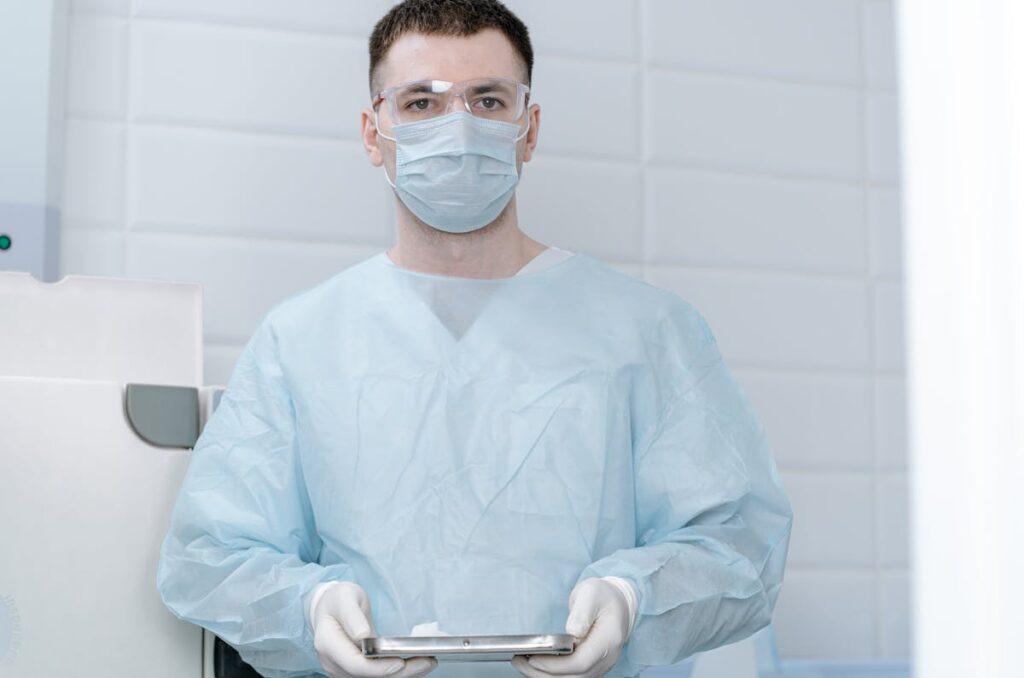 Doctor in a Surgical Mask and Scrubs Standing wiht Medical Instruments in his Hands